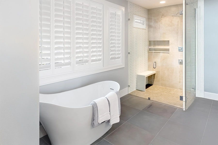 Enjoy pristine Polywood shutters in your bathroom for years without worrying about water stains or mold. White Polywood shutters on a large window over a freestanding tub