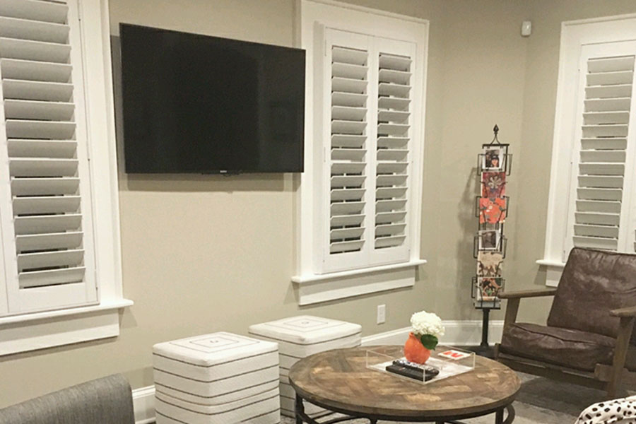 White Polywood shutters on windows in a room with a TV on the wall